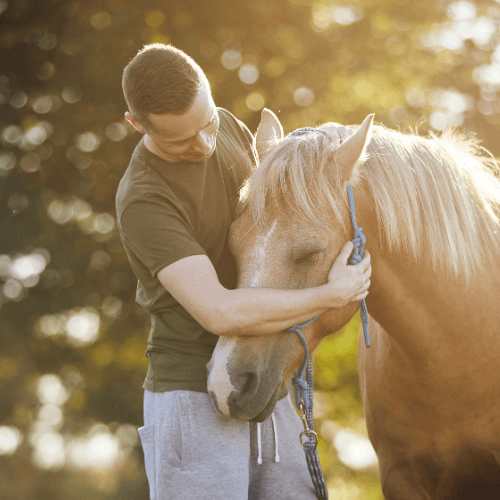 A man with his arm around the horses head bonding with it. 